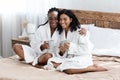 Happy besties in bathrobes sitting on bed, smiling at camera Royalty Free Stock Photo