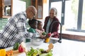 Happy african american grandparents and grandchildren washing vegetables in kitchen, slow motion