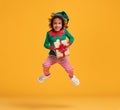 Happy african american kid boy Christmas elf costume with wrapped Xmas gift in hands jumping in air Royalty Free Stock Photo