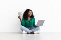 Happy african american lady gambling online, holding laptop and money Royalty Free Stock Photo