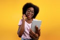 Happy african american lady using smartphone and making video call, smiling at cellphone camera over yellow background Royalty Free Stock Photo