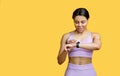 Happy african american lady using smartwatch to monitor progress, checking her performance, yellow background