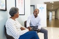 Happy african american male doctor using tablet and talking with senior woman in hospital Royalty Free Stock Photo