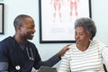 Happy african american male doctor using tablet and talking with senior woman in hospital Royalty Free Stock Photo