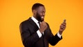Happy african-american male in suit receiving news on phone, making yes gesture