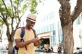 Happy african american man with bag and hat walking with mobile phone outdoors Royalty Free Stock Photo