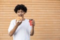 A happy African-American man biting an orange donut and holding a cup of coffee Royalty Free Stock Photo