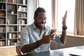 Happy African American man excited by good news, using phone