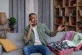 Happy african american man having phone call while packing clothes into travel bag, preparing for summer vacation Royalty Free Stock Photo