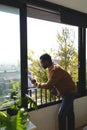 Happy african american man looking through window and using smartphone Royalty Free Stock Photo