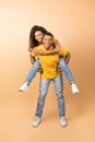 Happy african american man piggybacking his cheerful girlfriend, having fun together over peach background, full length Royalty Free Stock Photo
