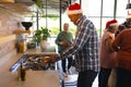 Happy african american man in santa hat preparing meal with friends in sunny kitchen at home Royalty Free Stock Photo