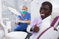 Happy african american man sitting in dental chair after teeth cure giving thumb up Royalty Free Stock Photo