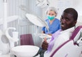 Happy african american man sitting in dental chair after teeth cure giving thumb up Royalty Free Stock Photo