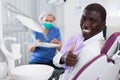 Happy african american man sitting in dental chair after teeth cure giving thumb up Royalty Free Stock Photo