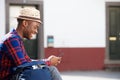 Happy african american man sitting outside and looking at mobile phone Royalty Free Stock Photo