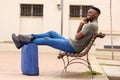 Happy african american man sitting outside with suitcase and talking on cell phone Royalty Free Stock Photo