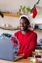 Happy african american man wearing santa hat, using laptop for video call Royalty Free Stock Photo