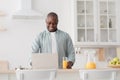 Happy african american mature man drinking orange juice and watching movie on laptop in kitchen Royalty Free Stock Photo