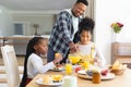 Happy african american man pouring orange juice to glass at table at home, copy space Royalty Free Stock Photo