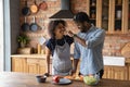 Happy African American man feeding wife, cooking salad together