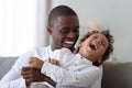 Happy african american millennial father tickling laughing son.