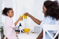 happy african american mom and daughter clinking glasses with orange