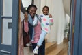 Happy african american mother with daughter in arms standing in doorway and raising hand