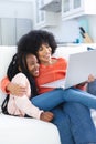 Happy african american mother and daughter embracing on couch and using laptop at home, copy space Royalty Free Stock Photo