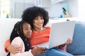 Happy african american mother and daughter embracing on couch and using laptop at home, copy space Royalty Free Stock Photo