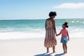 Happy african american mother and daughter holding hands while standing at beach on sunny day Royalty Free Stock Photo