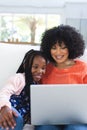 Happy african american mother and daughter sitting on couch and using laptop at home, copy space Royalty Free Stock Photo