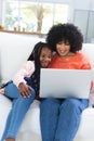 Happy african american mother and daughter siyying on couch and using laptop at home, copy space Royalty Free Stock Photo