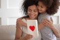 Happy african american mother hugging daughter, holding greeting card. Royalty Free Stock Photo