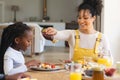 Happy african american mother pouring maple syrup on fruits in dining room at home, copy space