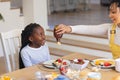 Happy african american mother pouring maple syrup on fruits in dining room at home, copy space