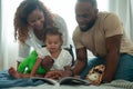 Happy African American Parents with little daughters playing , reading book on the bed in bedroom at home, happy family concept Royalty Free Stock Photo