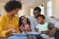 Happy African American parents with their cute children reading storybook on the sofa