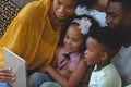 Happy African American parents with their cute children using digital tablet on sofa Royalty Free Stock Photo