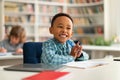 Happy african american primary school boy sitting at desk in classroom, writing in notebook and smiling, free space Royalty Free Stock Photo