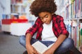 Happy african american schoolboy reading book sitting on floor in school library Royalty Free Stock Photo