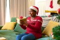 Happy african american senior woman in santa hat opening present at christmas time Royalty Free Stock Photo