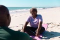 Happy african american senior woman talking with man while relaxing on mats at beach in summer Royalty Free Stock Photo