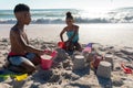 Happy african american siblings making sandcastle together at beach on sunny day Royalty Free Stock Photo