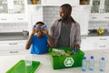 Happy african american son sorting recycling with father in kitchen, playing with plastic bottles Royalty Free Stock Photo