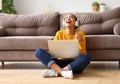 Happy african american teen girl in headphones sitting on floor and listening music while working remotely or studying online Royalty Free Stock Photo