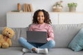Happy african american teen girl using laptop computer, browsing internet on sofa at home Royalty Free Stock Photo