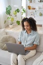 Happy African American teen girl using laptop computer sitting on sofa at home. Royalty Free Stock Photo