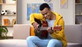 Happy African-American teenager playing guitar, enjoying favorite hobby, leisure