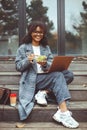 Happy african american woman eating green salad while working on laptop outdoors on fall day Royalty Free Stock Photo